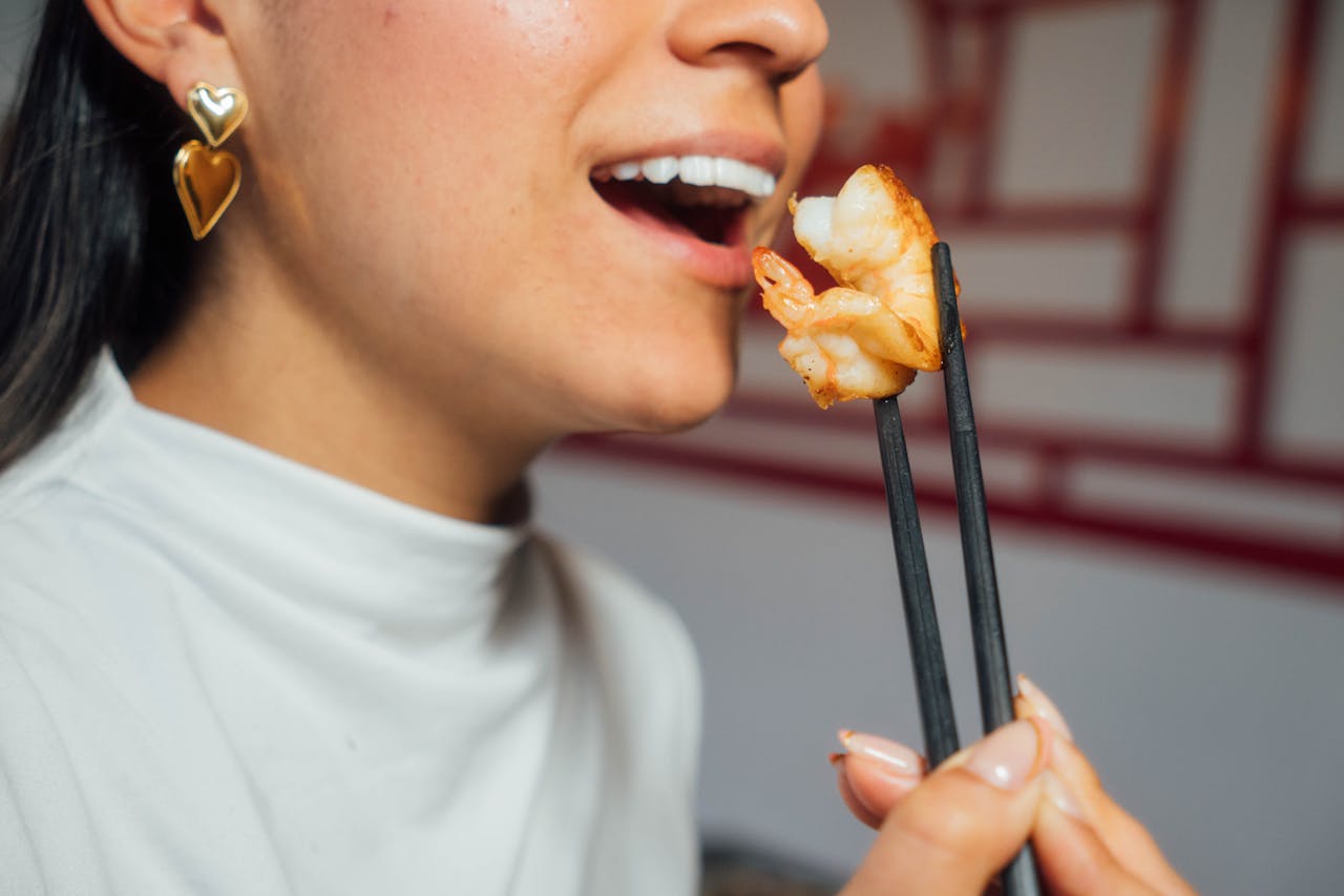 Woman enjoying shrimp with chopsticks, highlighting culinary experience and style.